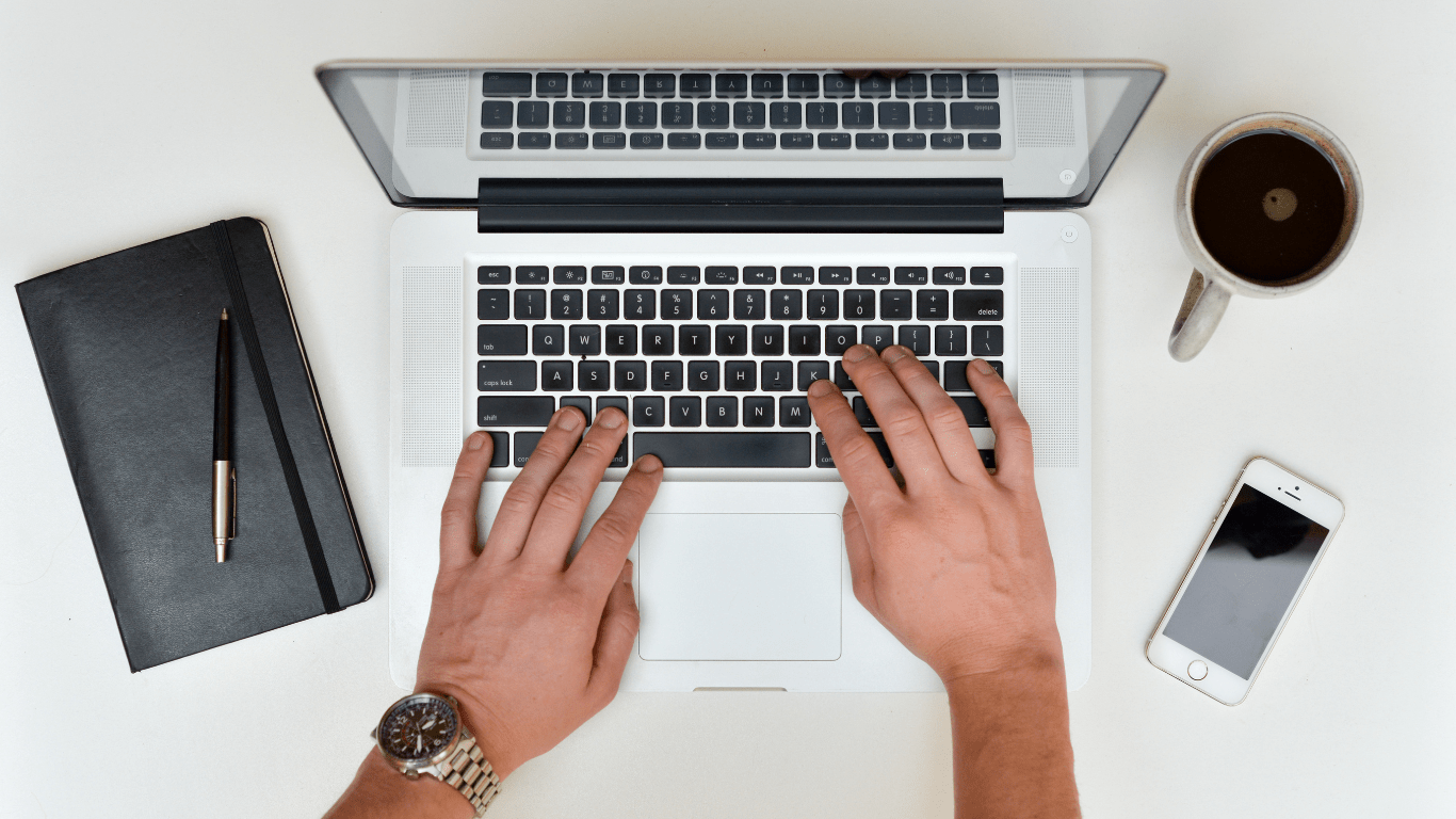 a person typing on a laptop with a cup of coffee next to it