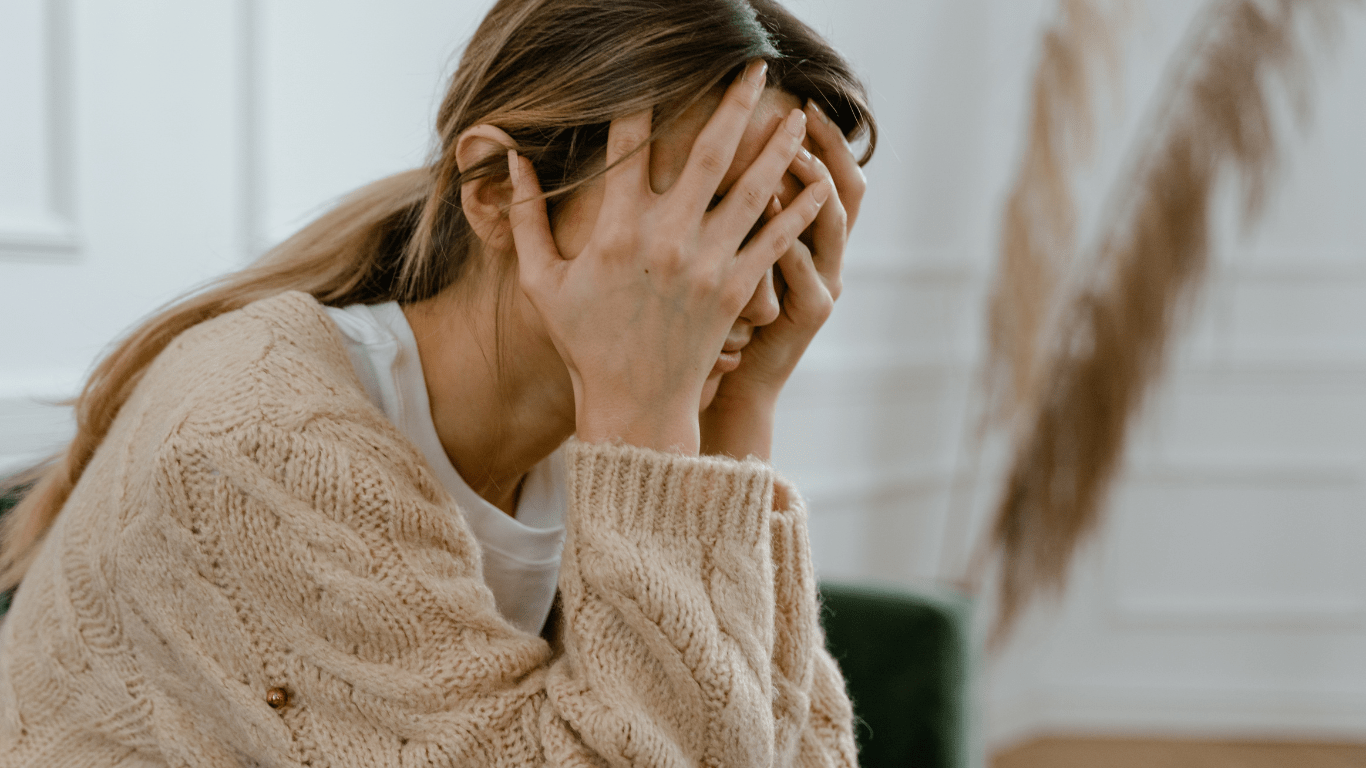 a person covers their face with their hands while sitting on a couch