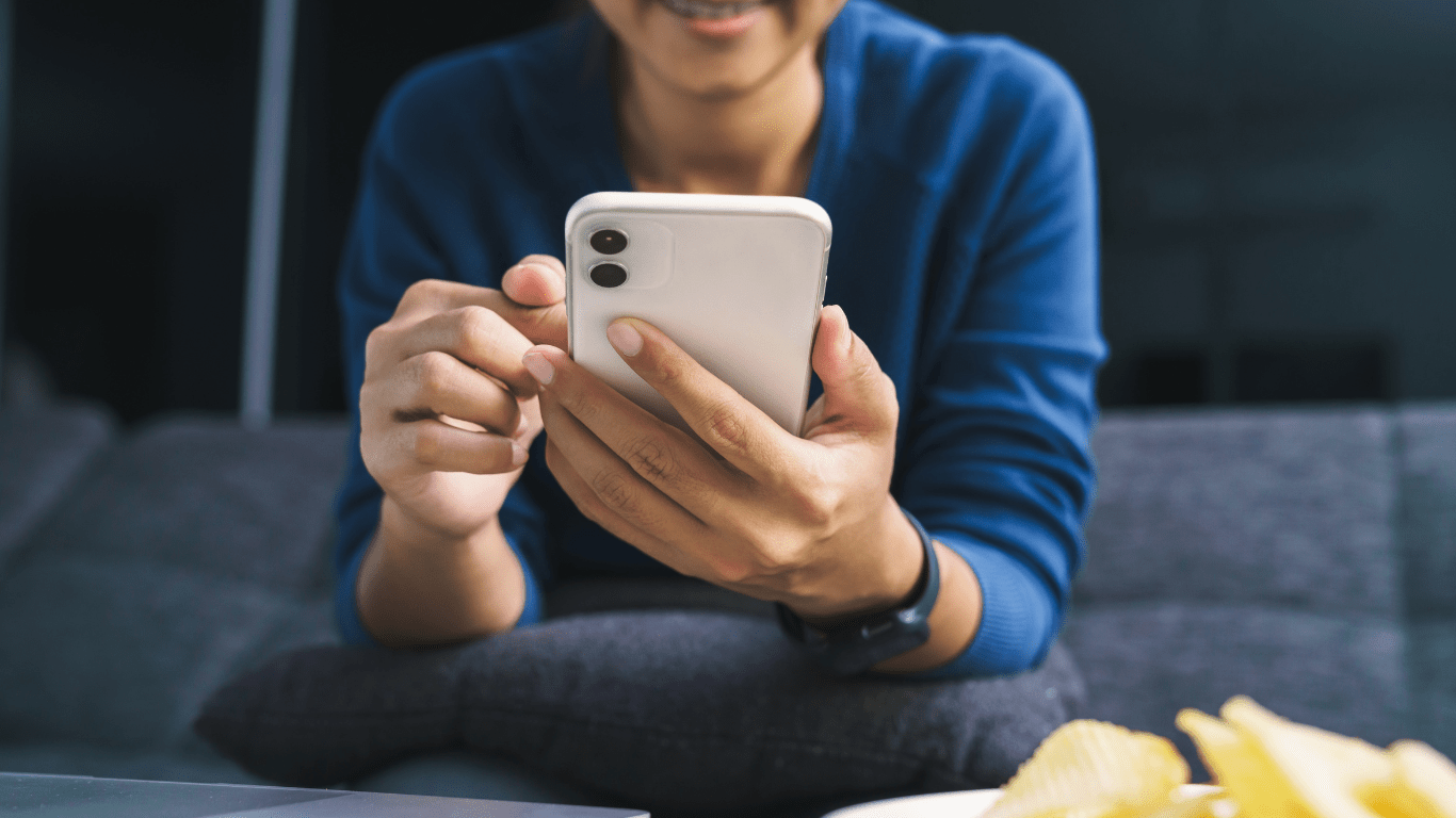 a person sitting on a couch holding a cell phone and looking at it