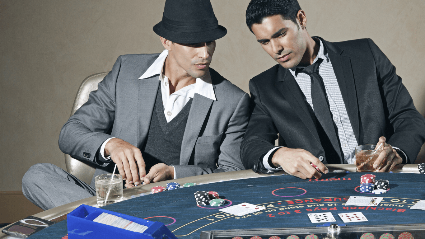 Two individuals in suits playing blackjack at a casino table.