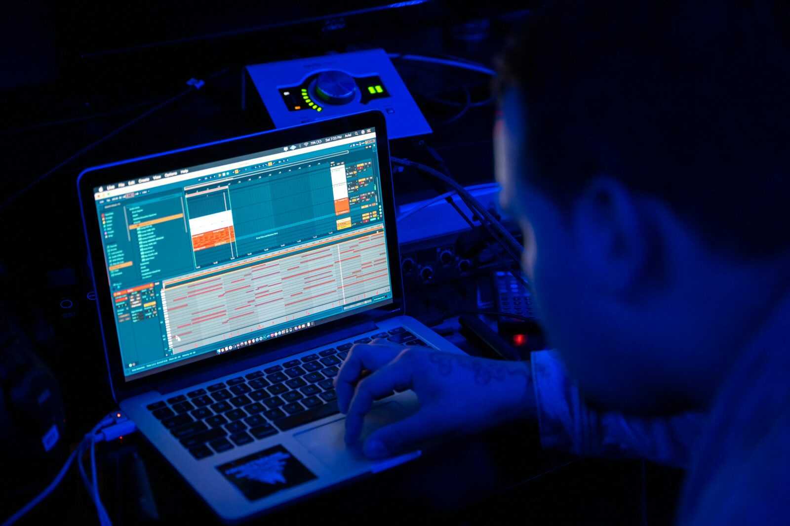 Focused man working on a laptop in a dimly lit tech environment.